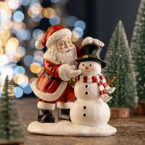 Aynsley Santa and Snowman resin figurine, featuring Santa Claus in a classic red suit adjusting a smiling snowman's black top hat against a blurred bokeh Christmas light background.