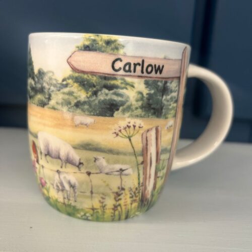 • A Shannonbridge Pottery ceramic mug with a painted Irish countryside scene featuring sheep, robins, and a signpost reading Carlow.
