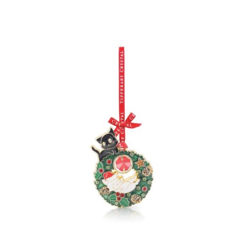 e holiday ornament features an intricate green enamel Christmas wreath accented with golden stars and pinecones, a sleeping white cat wearing a Santa hat nestled in the center, and a wide-eyed black cat perched on top. A vibrant red ribbon printed with "Tipperary Crystal" is tied in a neat bow at the top for hanging.