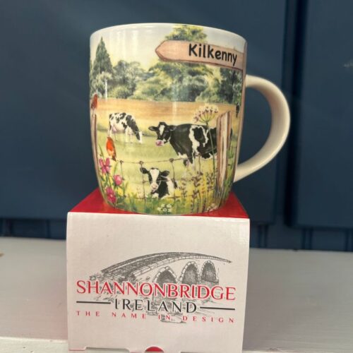 A Shannonbridge Pottery ceramic mug with a painted Irish countryside scene featuring sheep, robins, and a signpost reading Kilkenny.